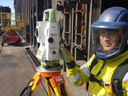 Surveyor with Leica robot total station in chemical plant; gas detection and face protection required.